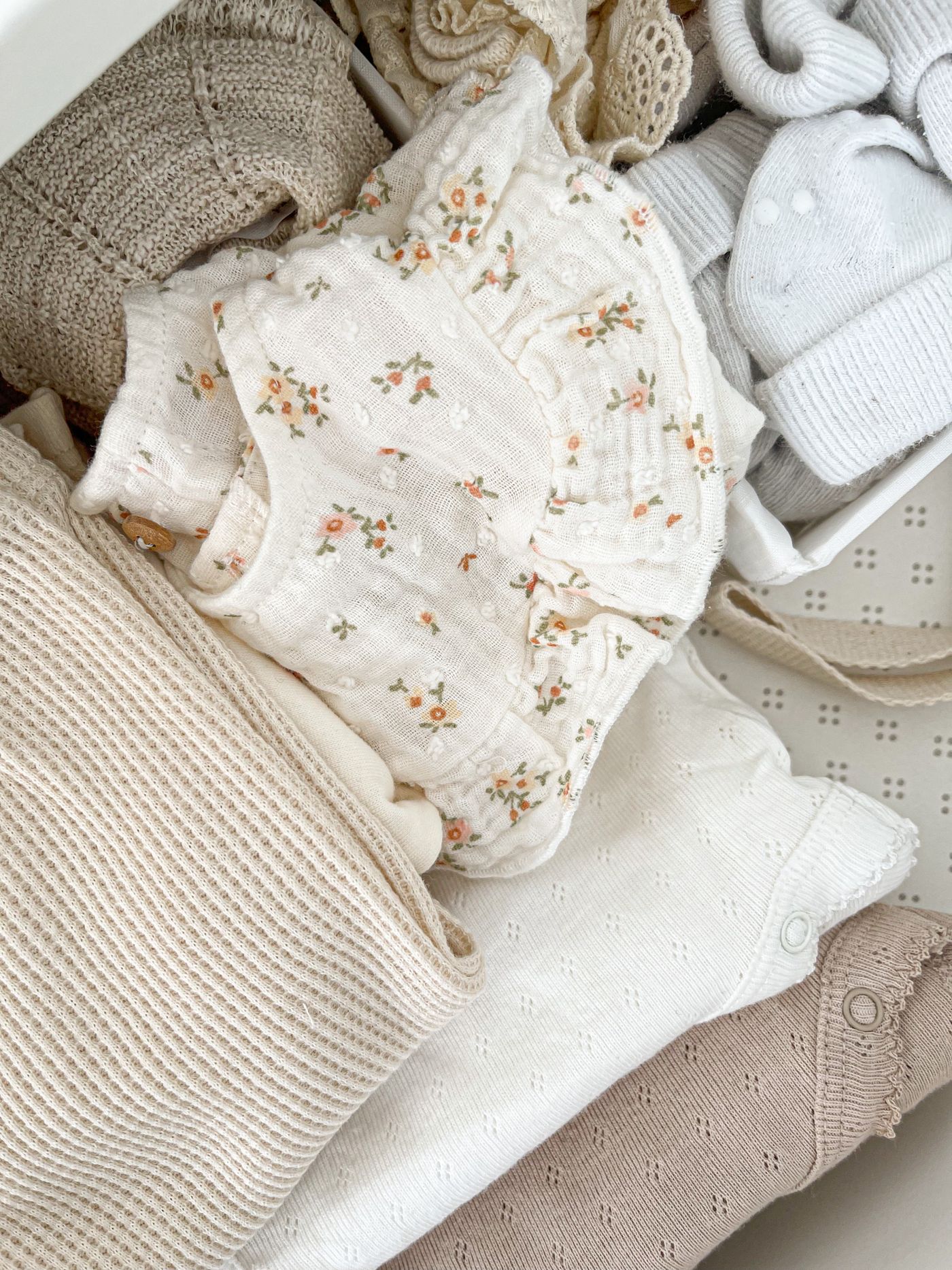 Folded neutral baby clothes and muslins