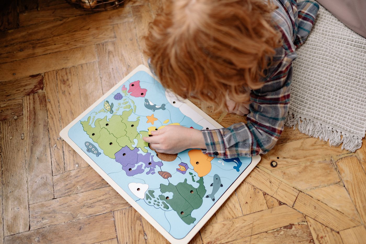 Child putting together a wooden world map puzzle on the floor